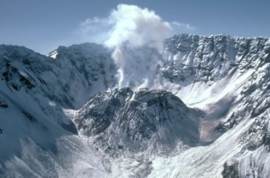 A mountain with snow and a cloud of smoke. Mt. St. Helens in Washington State, its rhyolite in composition and erupted in 1980. Description automatically generated