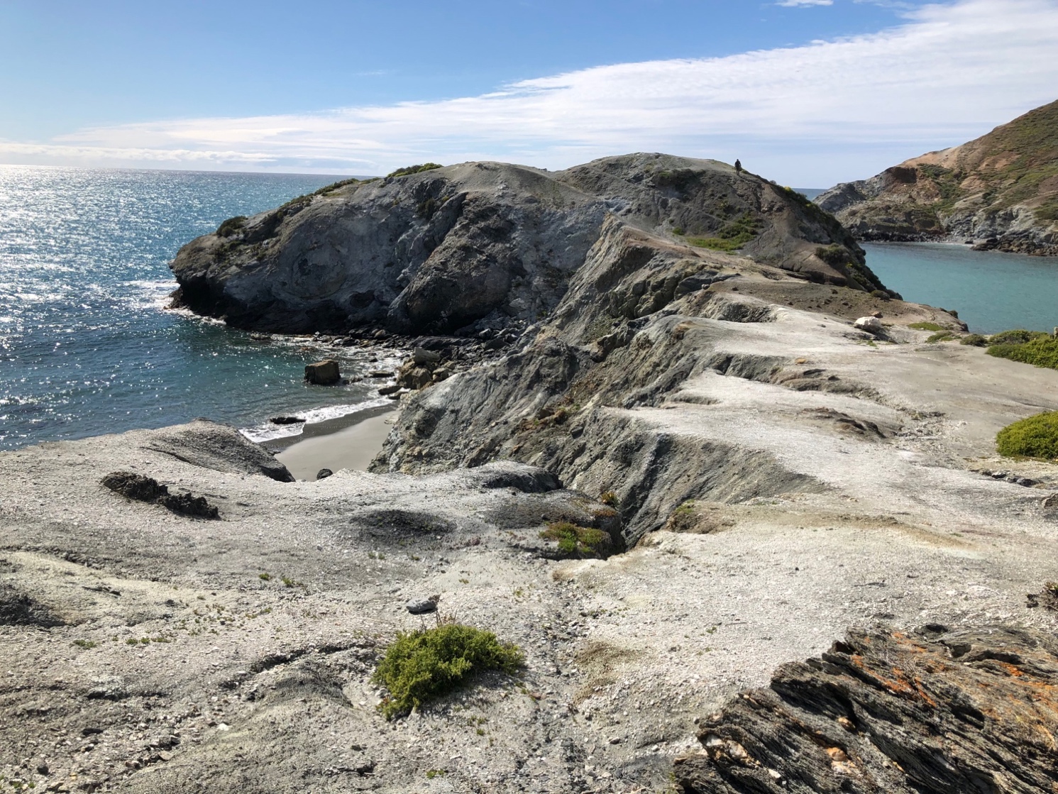 A rocky coastline with a body of water. The blueschist whale tail and greenschist in the lower right,