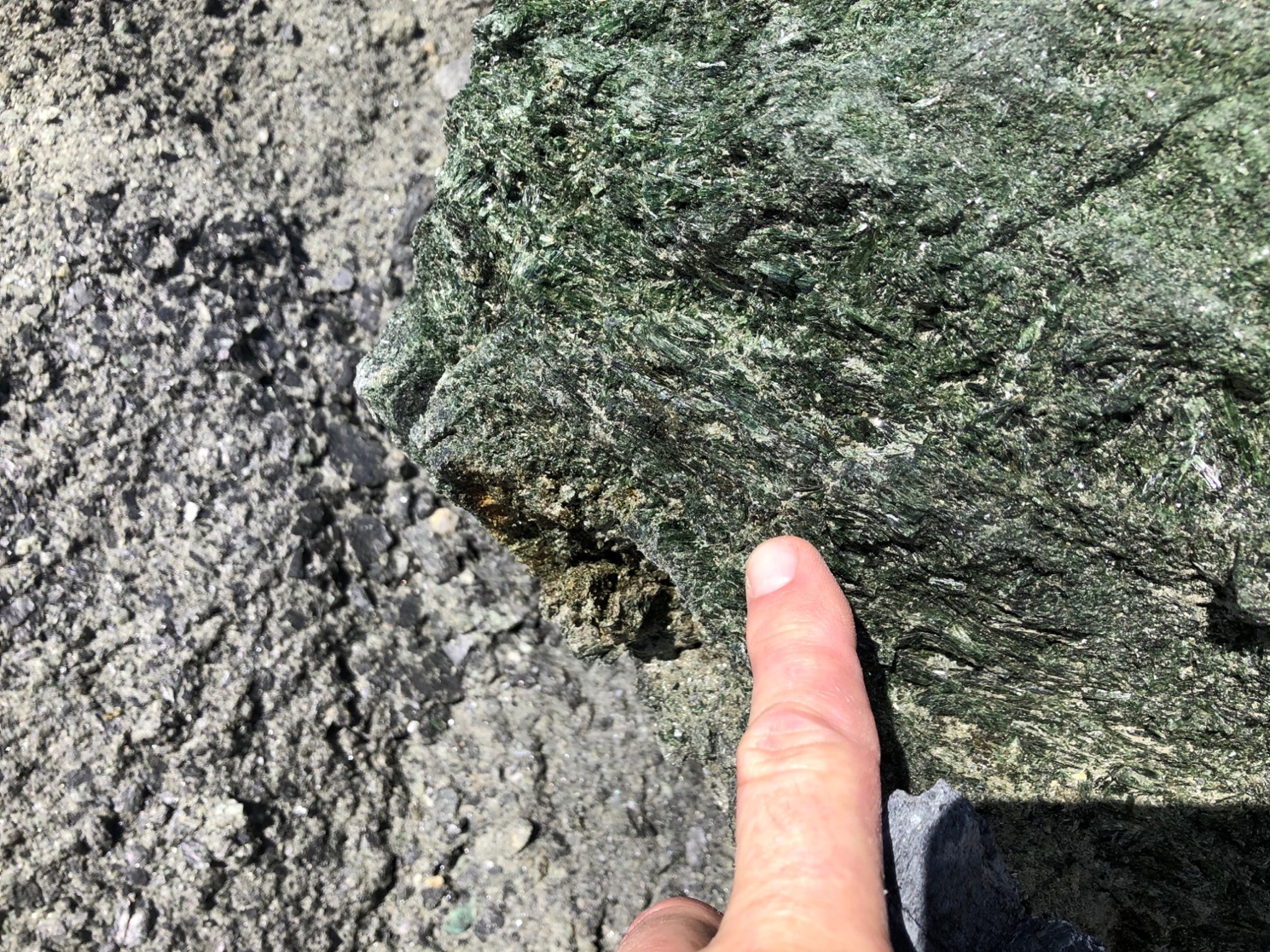 A finger touching a rock, greenstone with epidote/actinolite.